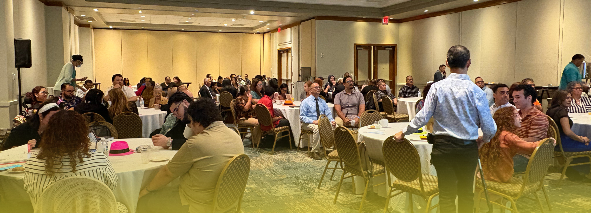 Salón de conferencias con múltiples mesas redondas donde personas diversas, incluyendo personas con y sin impedimentos, participan activamente en el Foro de Vida Independiente. Los asistentes están sentados escuchando, dialogando y compartiendo en un ambiente inclusivo y organizado, celebrado en el Embassy Suites de Dorado.