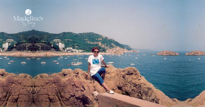 Madeline Witch sin glasses sitting on rocky cliffs overlooking the sea in Calella de la Costa, Spain, capturing a moment of travel, freedom, and reflection.
